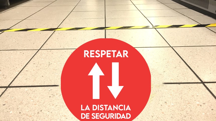 Adhesivo rojo redondo en el suelo con flechas blancas hacia arriba y abajo y texto respectar la distancia de seguridad
