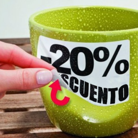 taza apoyada sobre una mesa con una mano retirando una etiqueta personalizada removible con el porcentaje de descuento