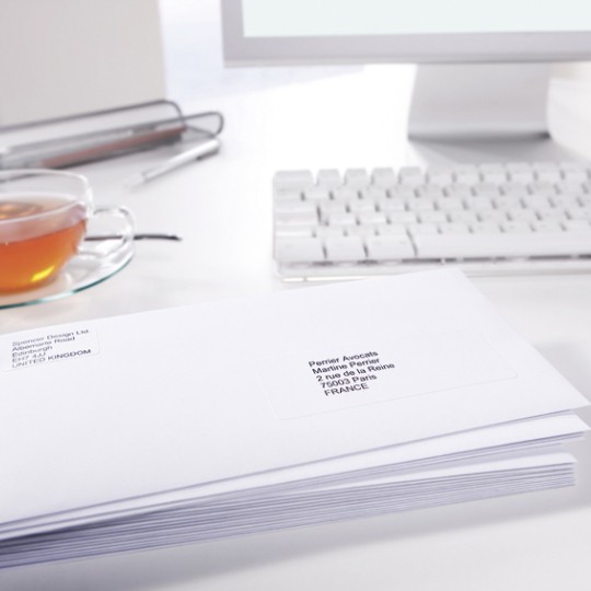 Escritorio con té y ordenador con una pila de sobres con etiquetas de envío en primer plano