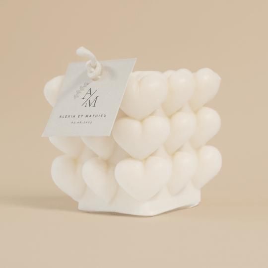 Una vela blanca con corazones en relieve para bodas. La vela lleva una etiqueta colgantes cuadrada personalizada