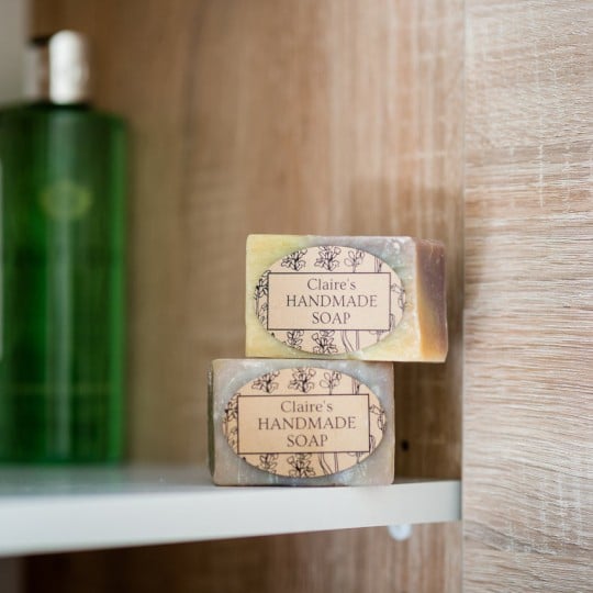 Primer plano de dos pastillas de jabón artesanal con etiquetas ovaladas personalizadas en estantería