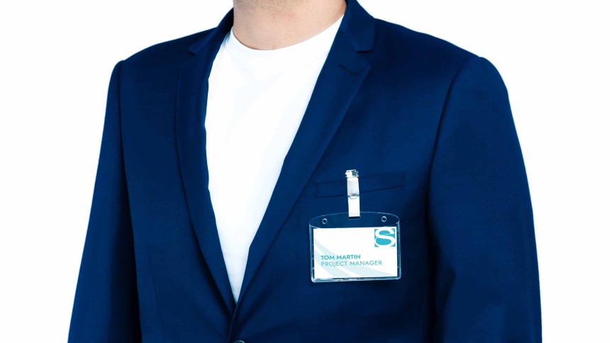 Hombre con blazer azul y camisa blanca, llevando un portanombres con clip con su nombre