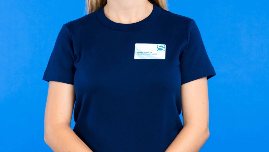 Mujer con camiseta azul llevando un identificativo adhesivo con su nombre, fondo azul