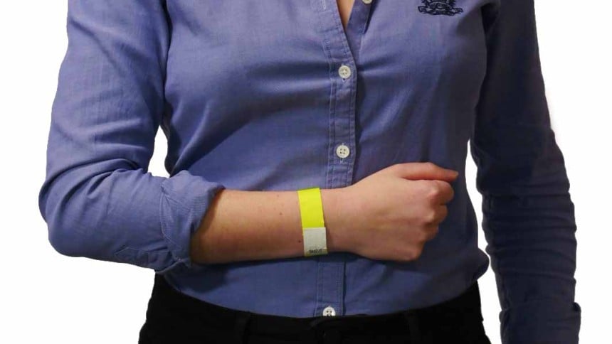 Mujer con camisa azul y pantalón negro, lleva una pulsera identificativa amarilla brillante en la muñeca izquierda