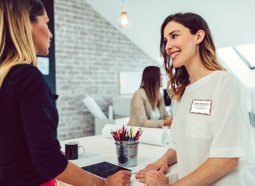 Dos mujeres conversando en una oficina. Una de ellas lleva un identificativo adhesivo con su nombre en su camisa