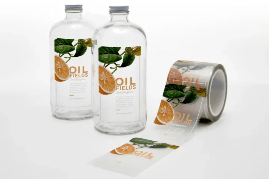 Dos botellas con etiquetas transparentes impermeables. Al lado un rollo de etiquetas trasparentes para frascos de vidrio