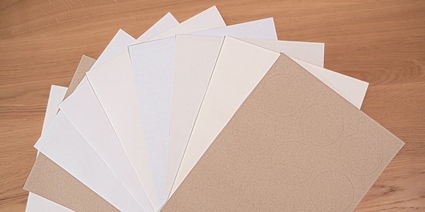 Varias hojas de papel de diversos materiales dispuestas en forma de abanico sobre una mesa de madera