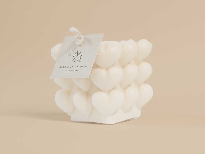 Una vela blanca con corazones en relieve para bodas. La vela lleva una etiqueta colgantes cuadrada personalizada
