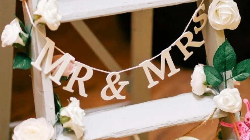 La imagen muestra una escalera blanca decorada con rosas blancas. Se encuentra una guirnalda con el texto MR & MRS