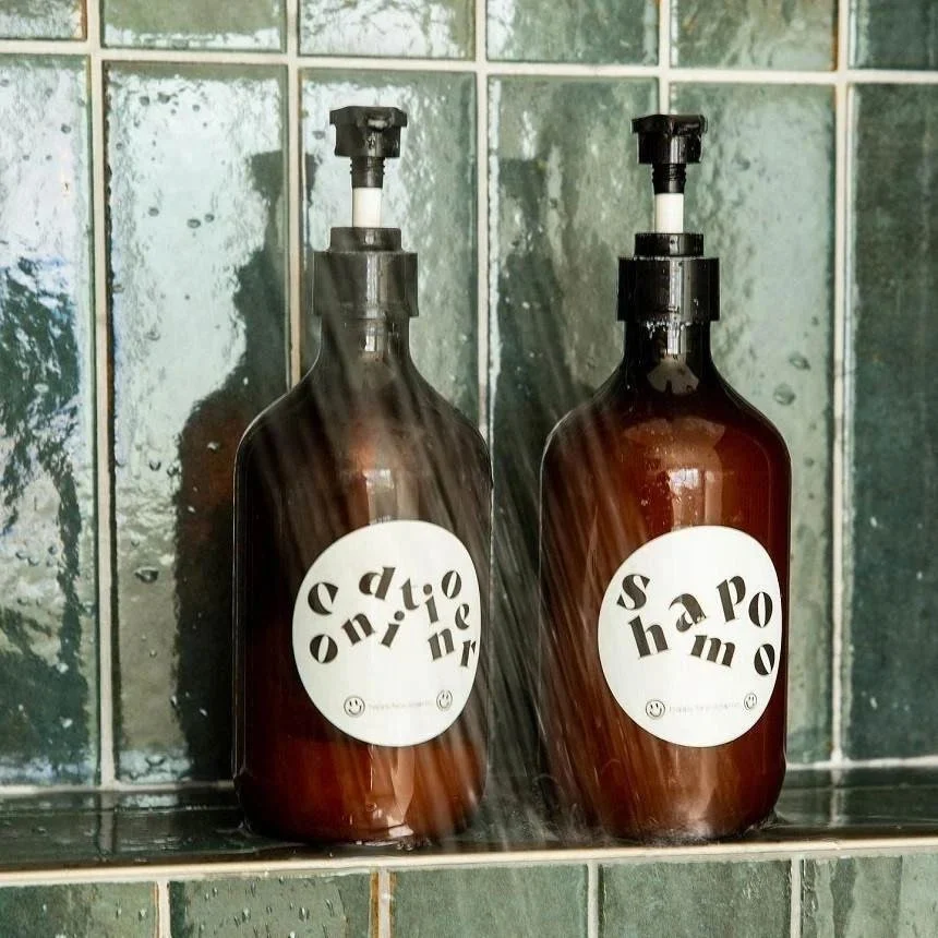 dos botes de champú colocados dentro de la ducha con etiquetas redondas impermeables personalizadas
