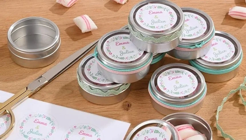 Pequeñas cajas de regalo con etiquetas "Emma & Julien" y confeti rosa. Tijeras y otras etiquetas sobre la mesa de madera.