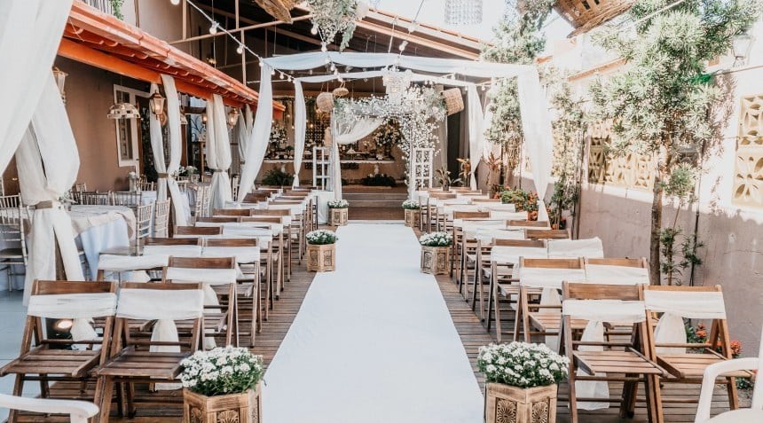 Ceremonia de boda al aire libre con sillas de madera, alfombra blanca, flores y dosel decorado