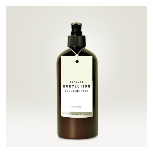 Una botella de loción corporal con etiqueta en inglés y alemán, indicada para piel seca, con un diseño simple y elegante.