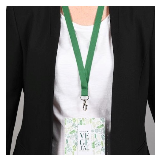 Una persona con una chaqueta negra y una camiseta blanca lleva un distintivo colgado con una cinta verde. El distintivo tiene un diseño relacionado con vegetales.