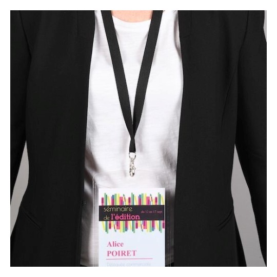 En la imagen se muestra una persona con una chaqueta negra y una camiseta blanca. Lleva un gafete de identificación que dice 'seminaire de l'édition', con el nombre 'Alice POIRET' y parece ser de un evento o seminario.