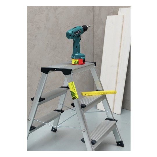La imagen muestra una escalera de aluminio con un destornillador colocado en ella. También hay una regla amarilla y algunas tablas de madera en el fondo.