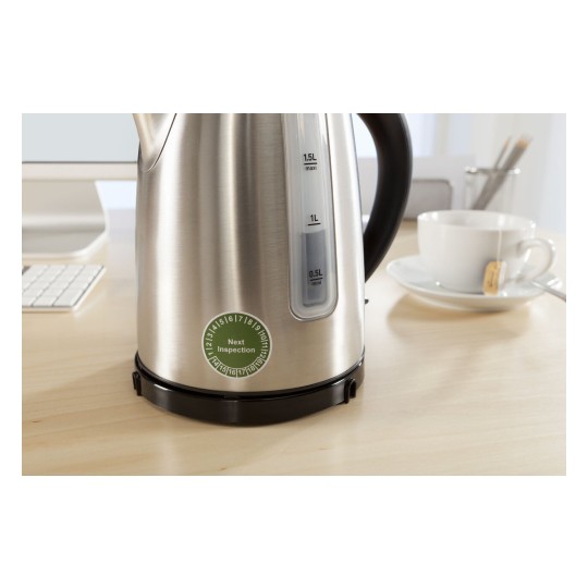 En la imagen hay una tetera eléctrica de acero inoxidable con una escala de medición de agua. También hay una taza blanca con un té y una mesa de madera clara.