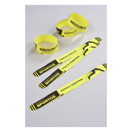En la imagen hay pulseras amarillas que indican seguridad y un evento deportivo, con nombres y cargos impresos.