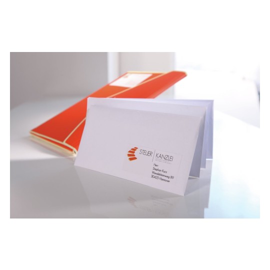 En la imagen se puede ver un sobre blanco con una tarjeta de presentación y un archivo de color naranja. El sobre lleva información de contacto sobre una firma de asesoría y está colocado sobre una superficie brillante.