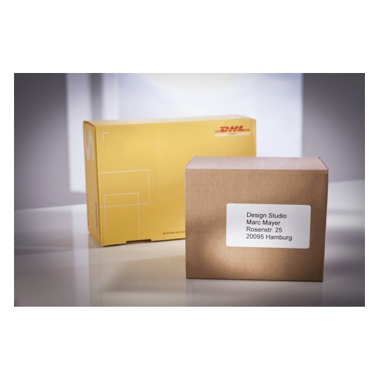 En la imagen se pueden ver dos cajas de envío, una amarilla de DHL y una marrón con una etiqueta que contiene una dirección específica.