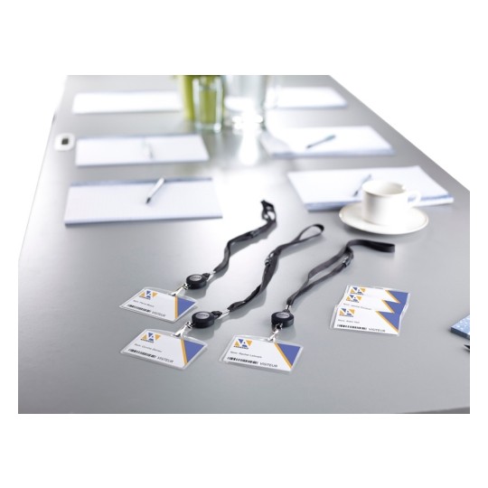 En la imagen se puede ver una mesa de reunión con blocs de notas, bolígrafos, un vaso de agua y varias tarjetas de identificación colgadas. Las tarjetas están etiquetadas como 'VISITEUR'.