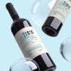 Dos botellas de vino con etiquetas con etiquetas envolventes personalizadas flotando sobre un fondo azul claro