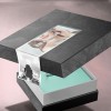 Caja de regalo negra parcialmente abierta con interior turquesa y una etiqueta con una foto de una mujer y texto