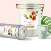 Tarro blanco con etiqueta  lata plateada con albaricoques, taza verde con bolsita de té y hoja tropical