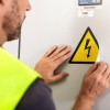 trabajador colocando una etiqueta adhesiva triangular que indica un cuadro eléctrico