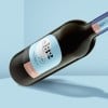 Botella de vino de vidrio con etiqueta adhesiva en forma de arco que describe el producto.
