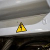 Etiqueta adhesiva triangular amarilla con un rayo que indica peligro de descarga eléctrica colocada en el borde metálico