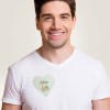 Hombre sonriendo con camiseta blanca, lleva un identificativo adhesivo en forma de corazón con su nombre