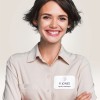 Mujer sonriendo con una camisa clara, lleva un identificativo adhesivo con su nombre