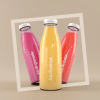 Botellas de tres colores morado, amarillo y naranja con etiquetas transparentes personalizadas