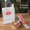 Un sobre con comida para llevar con etiqueta ovalada roja, lunch box y rollo de etiquetas ovaladas personalizadas