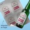 Botella de cerveza con etiqueta personalizada en forma de arco. Junto a ella, una hoja de etiquetas con la misma forma