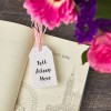 Libro abierto con etiqueta impresa «Tell Your Story» utilizada como marcapáginas y flores rosas de fondo.