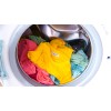 La imagen muestra una lavadora llena de ropa de varios colores, incluyendo una camiseta amarilla y otras prendas en tonos rosa y azul claro, girando dentro del tambor.