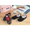En la imagen hay dos pares de zapatos: un par de zapatos de gato negro y un par negro simple. También hay una mochila rosa, una botella de agua, lápices y cuadernos en una superficie de madera.