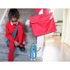 Una niña en escaleras con vestimenta roja, abrochándose un zapato. Tiene una mochila roja al lado. Hay un personaje animado al pie de la escalera.