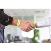 En la imagen se ven dos hombres dándose la mano, cada uno con una pulsera amarilla. El fondo sugiere un ambiente de oficina.
