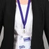 Una persona con un gafete que dice 'réunion GROUPE B' colgado de un cordón morado. La persona lleva una chaqueta negra y una camiseta blanca debajo.