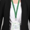 Una persona con una chaqueta negra y una camiseta blanca lleva un distintivo colgado con una cinta verde. El distintivo tiene un diseño relacionado con vegetales.