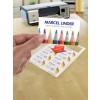 En la imagen se muestra una impresora, una persona sosteniendo una tarjeta que dice 'MARCEL LINDER ARTIST MATERIALS AND SUPPLIES', y una hoja impresa con varios diseños relacionados con materiales de arte.