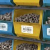 La imagen muestra estantes con cajas de plásticos que contienen tornillos y tuercas, etiquetados con el nombre de los artículos y sus ubicaciones en el almacén.
