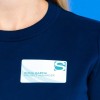 En la imagen se muestra a una persona que lleva una camiseta de color azul marino con una etiqueta en el pecho que dice 'Emma Garcia, Project Manager'.