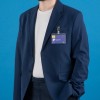 Una persona con un traje azul oscuro y una camiseta blanca, llevando un gafete con su nombre. El fondo es azul.