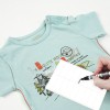 La imagen muestra una camiseta azul claro con un diseño gráfico y una etiqueta blanca donde se está escribiendo un nombre. La camiseta parece ser de niño o bebé.