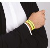 En la imagen se observa una mano que lleva una pulsera amarilla con la palabra 'SÉCURITÉ'. La pulsera parece ser de un evento o actividad deportiva, y la persona está vestida con un suéter oscuro sobre una camisa blanca.