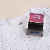 En la imagen hay una camiseta blanca con un estampado de puntos pequeños y un marcador de tela que dice 'TAMPON TEXTILE' de la marca Avery.